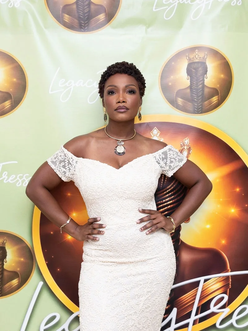 Christelle Bolden, founder of LegacyTress, in an ivory lace dress in front of the LegacyTress backdrop